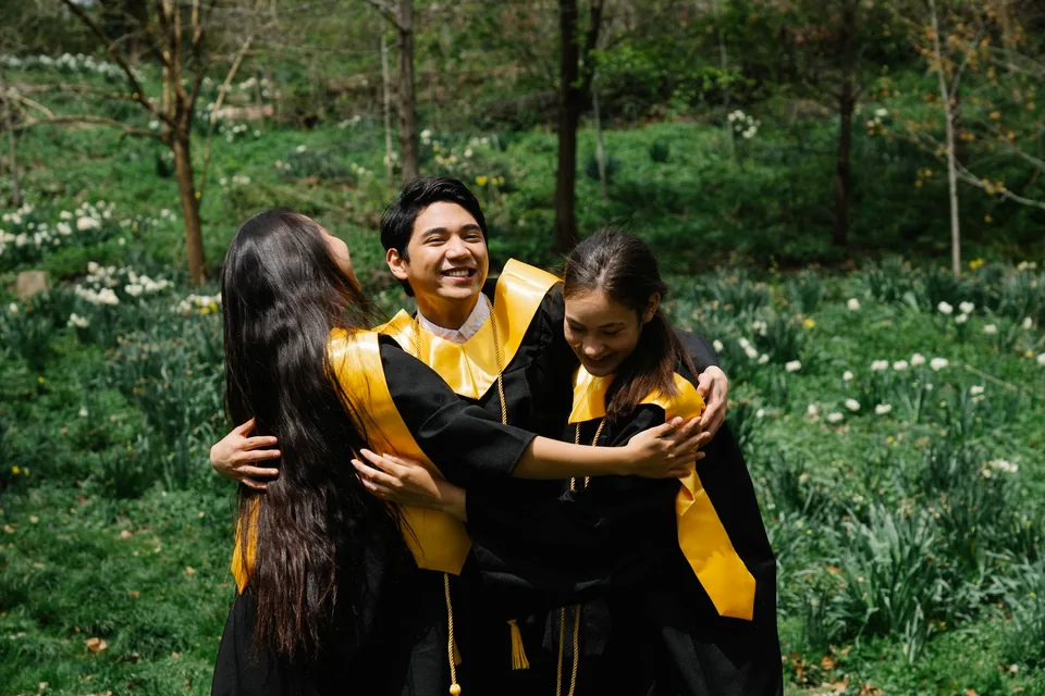 Three graduates in academic gowns celebrating outdoors