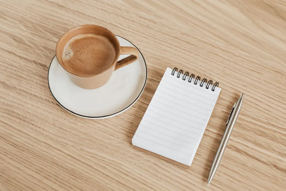 Blank notebook and pen beside a cup of coffee on a wooden desk
